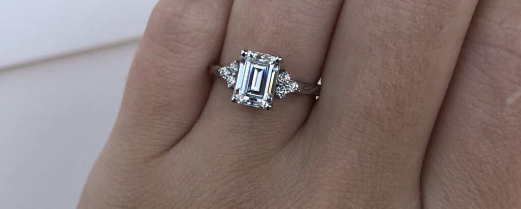 Custom emerald cut engagement ring with cluster sides in white gold on hand