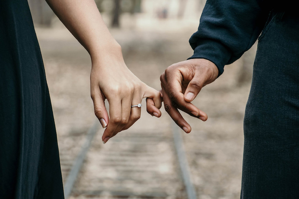 couple with pinkies intertwined and showing off engagement ring