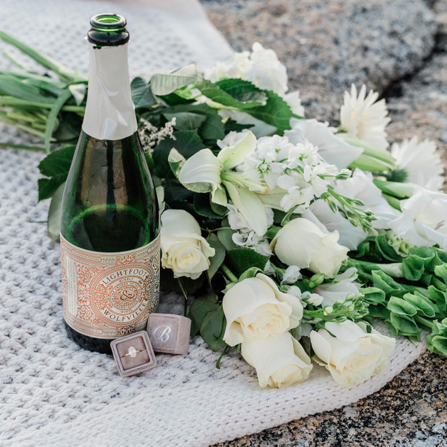 engagement ring in velvet ring box with white flowers and sparkling wine bottle