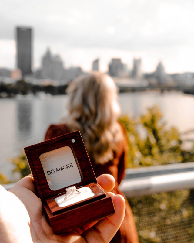 wooden ring box with engagement ring, skyline and woman in background