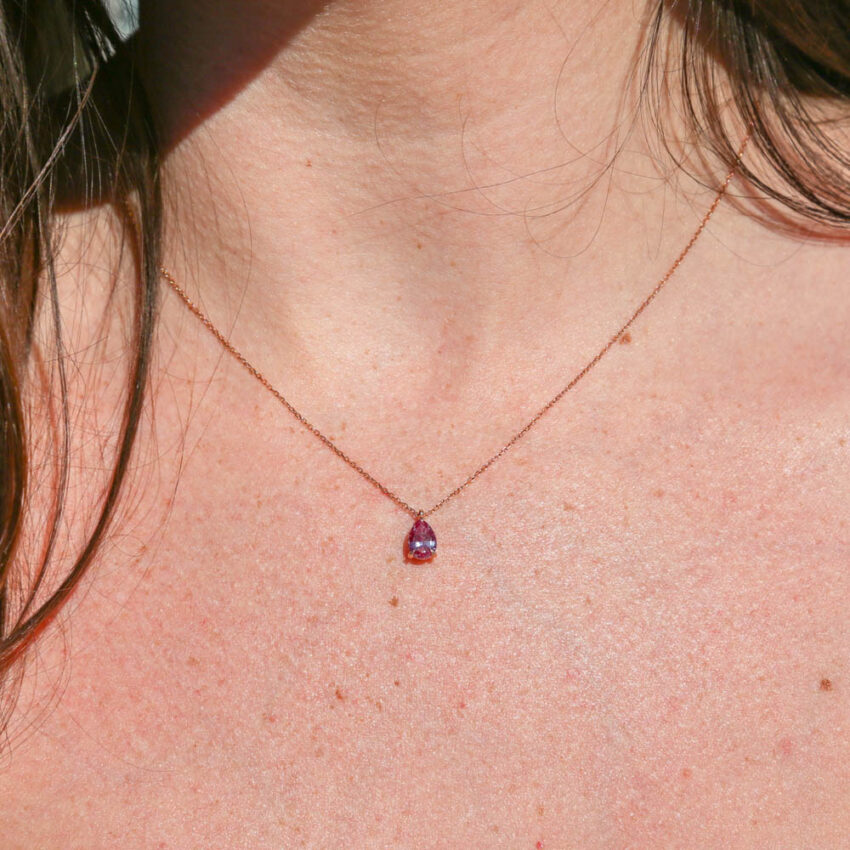 person wearing a rose gold necklace with a purple pear shaped pendant