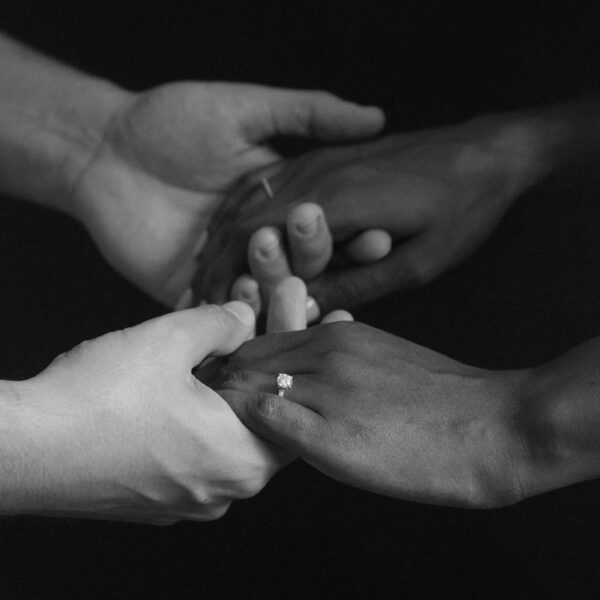 black and white photo of couple holding hands while showing off a round solitaire engagement ring