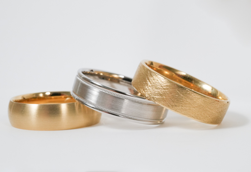 three mens wedding bands stacked on a white surface