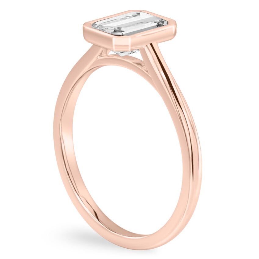 Angle view of emerald cut diamond bezel engagement ring in rose gold
