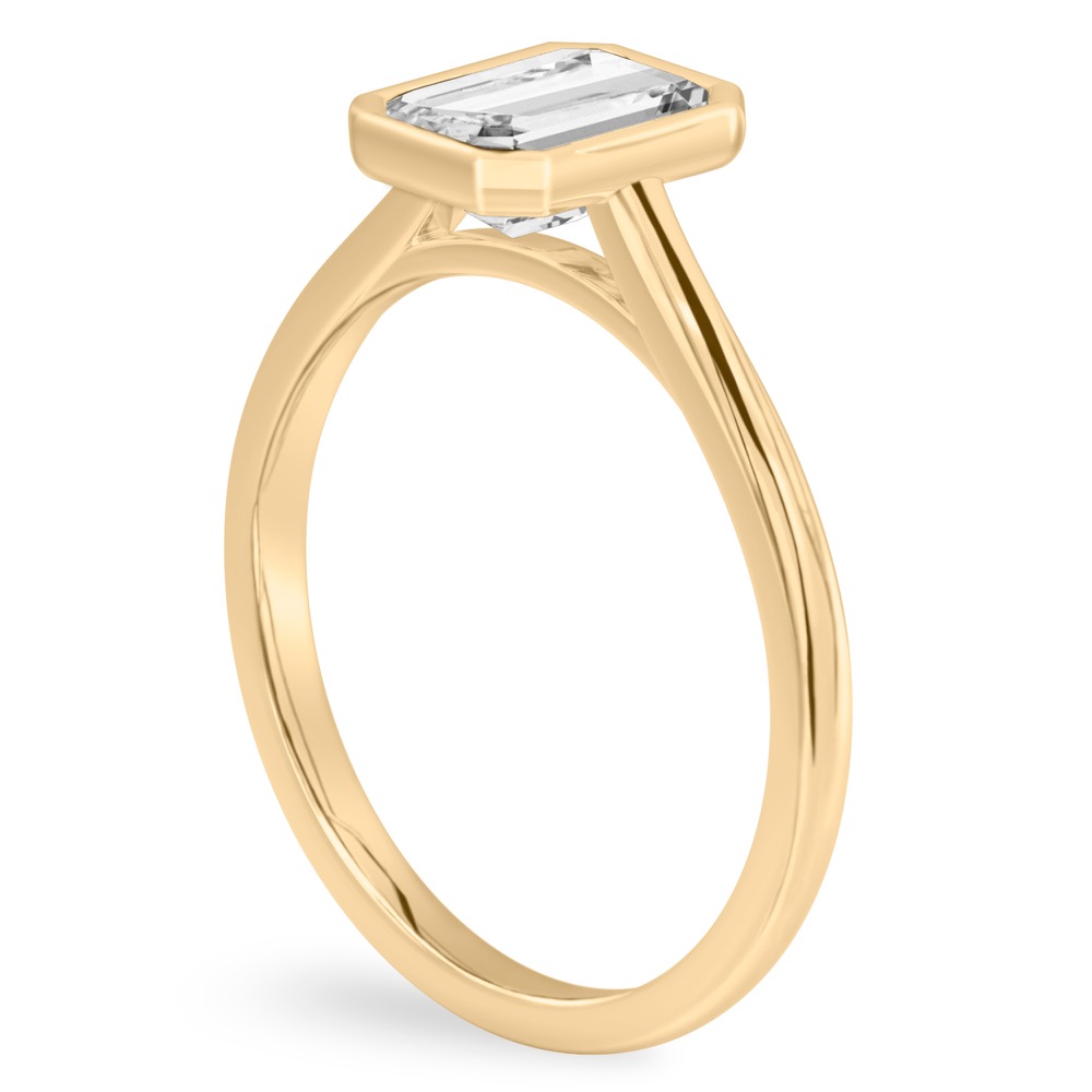 Angle view of emerald cut diamond bezel engagement ring in yellow gold