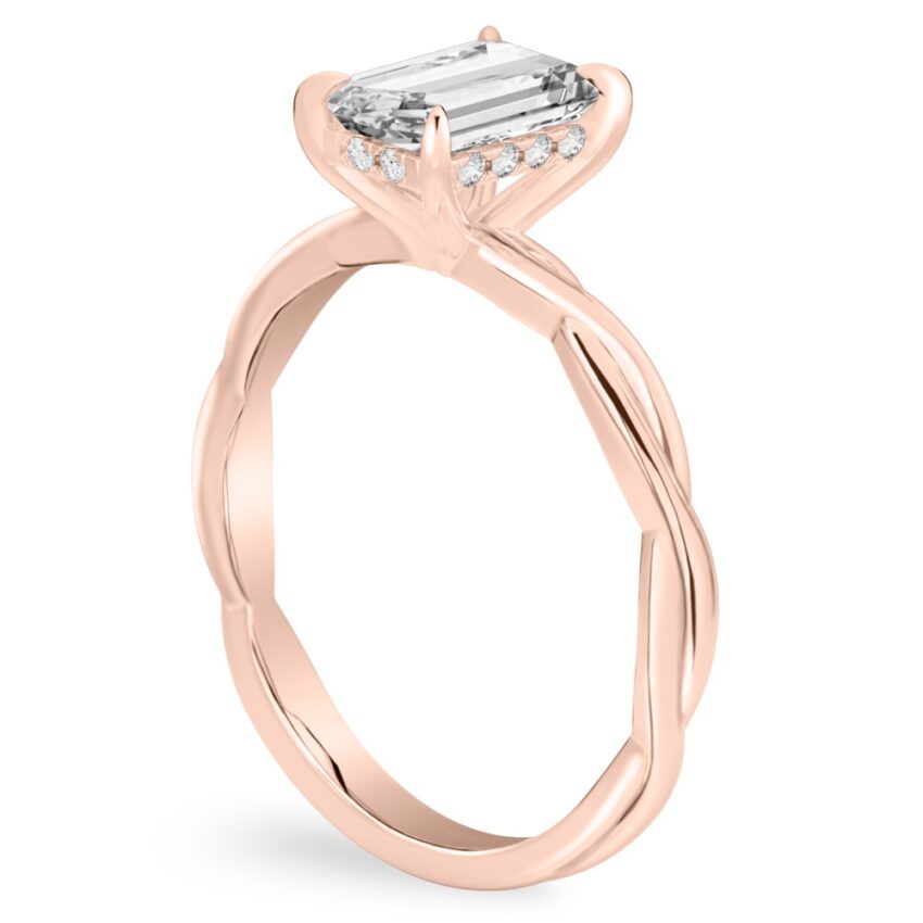 Angle view of emerald cut diamond twisted hidden halo engagement ring in rose gold