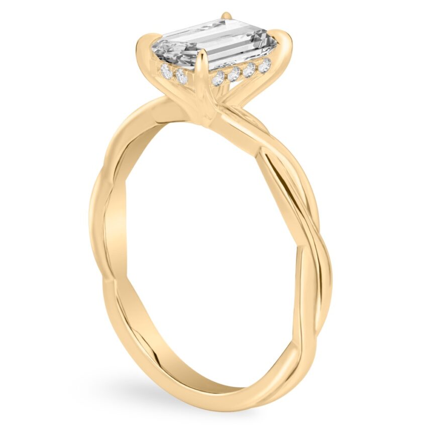Angle view of emerald cut diamond twisted hidden halo engagement ring in yellow gold