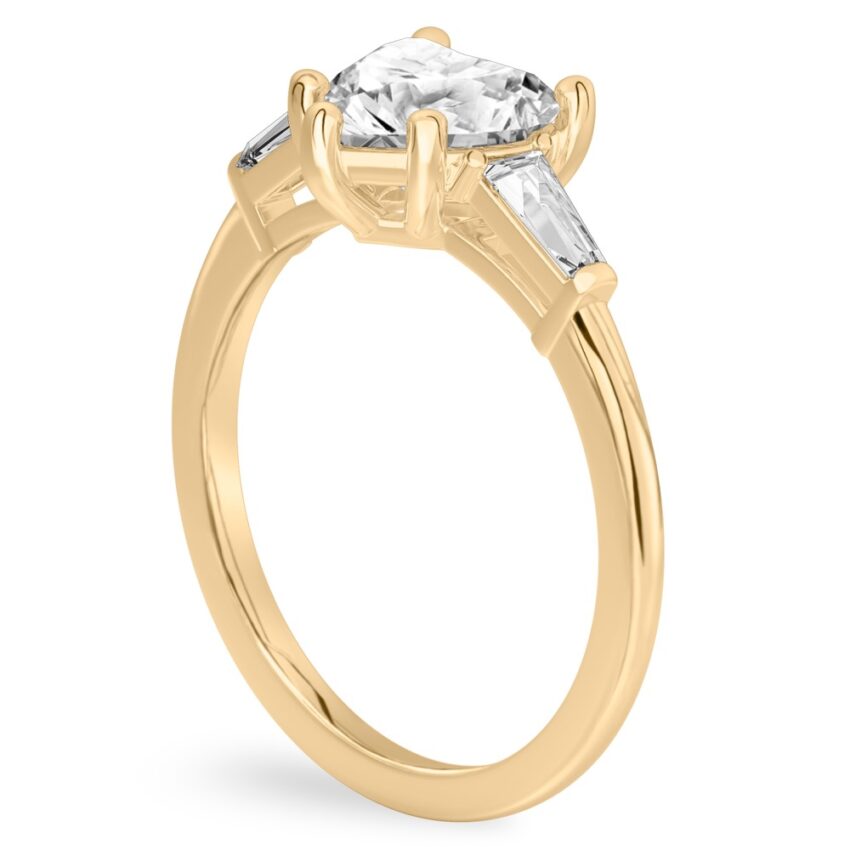 Angle view of heart shape diamond tapered baguette engagement ring in yellow gold