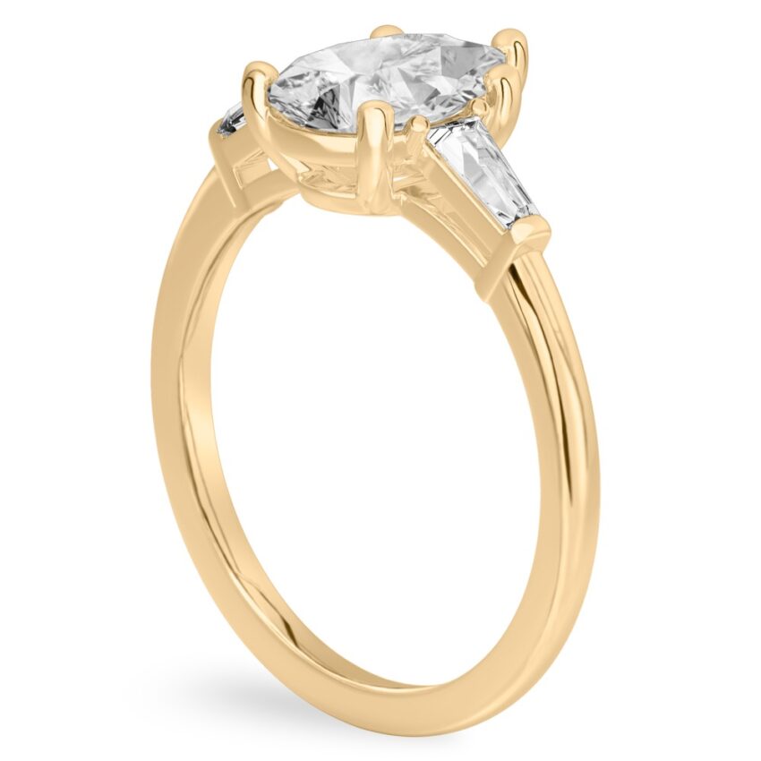 Angle view of pear shape diamond tapered baguette engagement ring in yellow gold