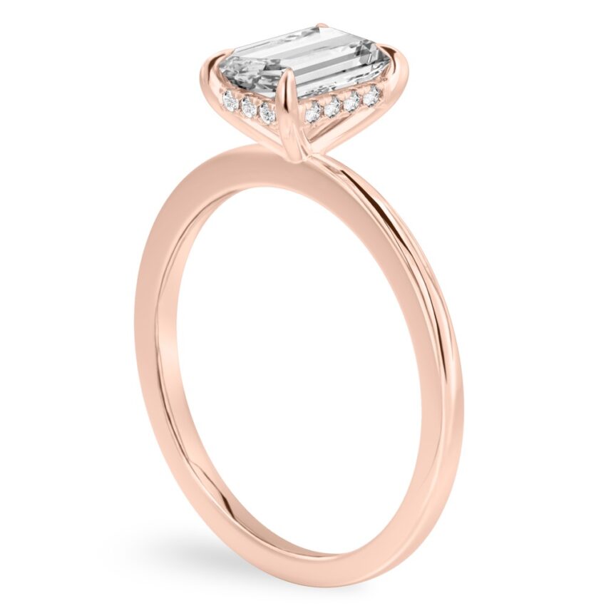 Angle view of emerald cut diamond hidden halo engagement ring in rose gold