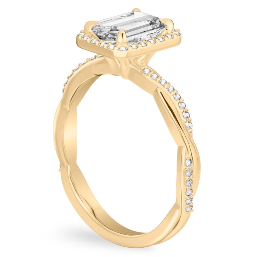 Angle view of emerald cut diamond twist halo engagement ring in yellow gold
