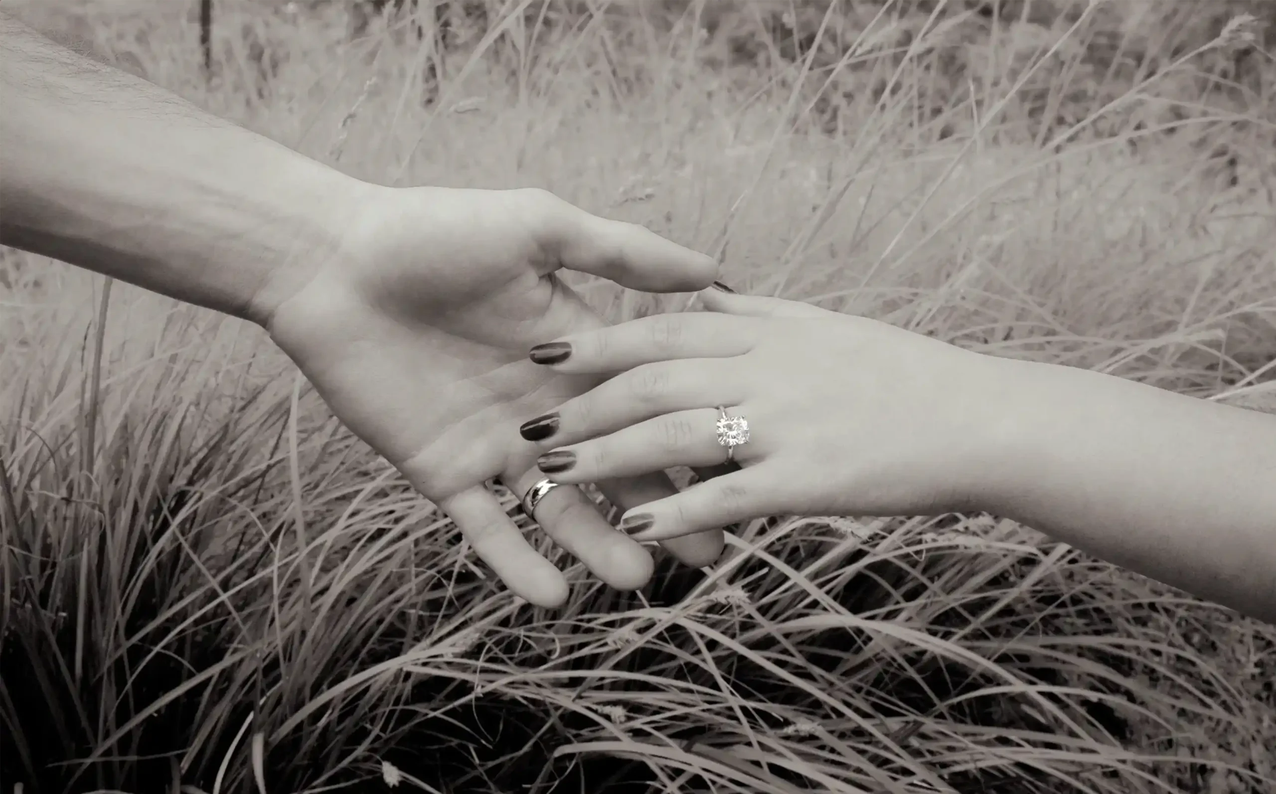 Couple holding hands in a field, highlighting a sparkling engagement ring for lifetime resizing.